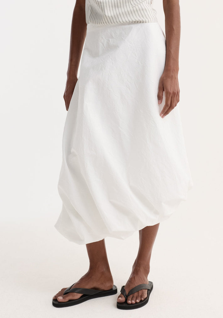 Model wearing Twisted crushed cotton skirt in optic white, featuring a voluminous bubble design and twist detail at hem, paired with black flip-flop sandals.