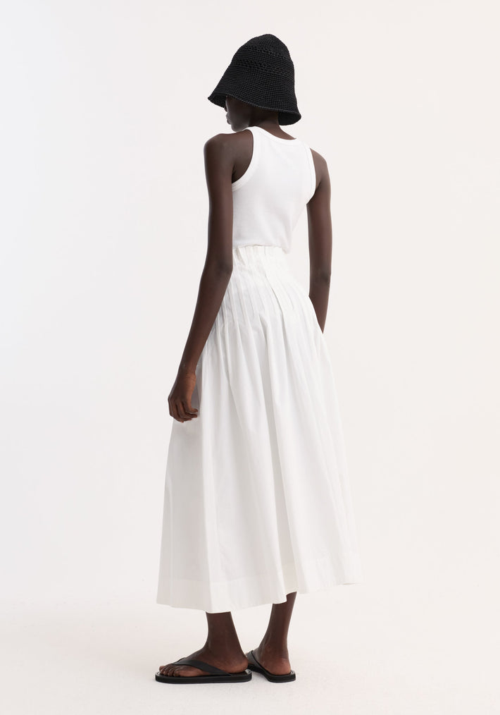 Rear view of model in a Pleated poplin maxi skirt, optic white, showcasing its high-waist pleated design with wide hem, paired with minimalist accessories.