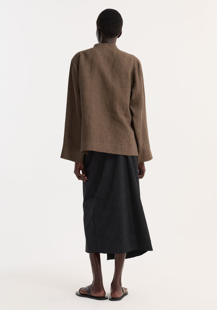 Person wearing a Sarong textured skirt | black, showcasing the back view with a knot detail and gathered fabric, paired with slide sandals.