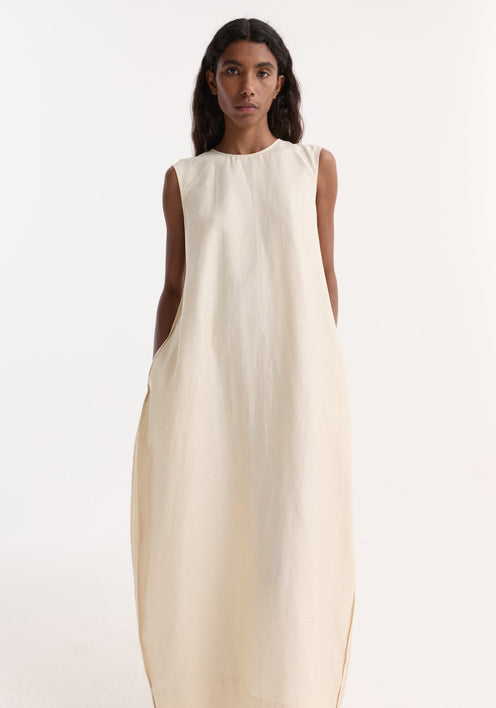Model in Hourglass linen silk dress | butter, featuring a sleeveless, floor-length design with a sculptural silhouette and subtle side pockets, paired with cream lace-up shoes.