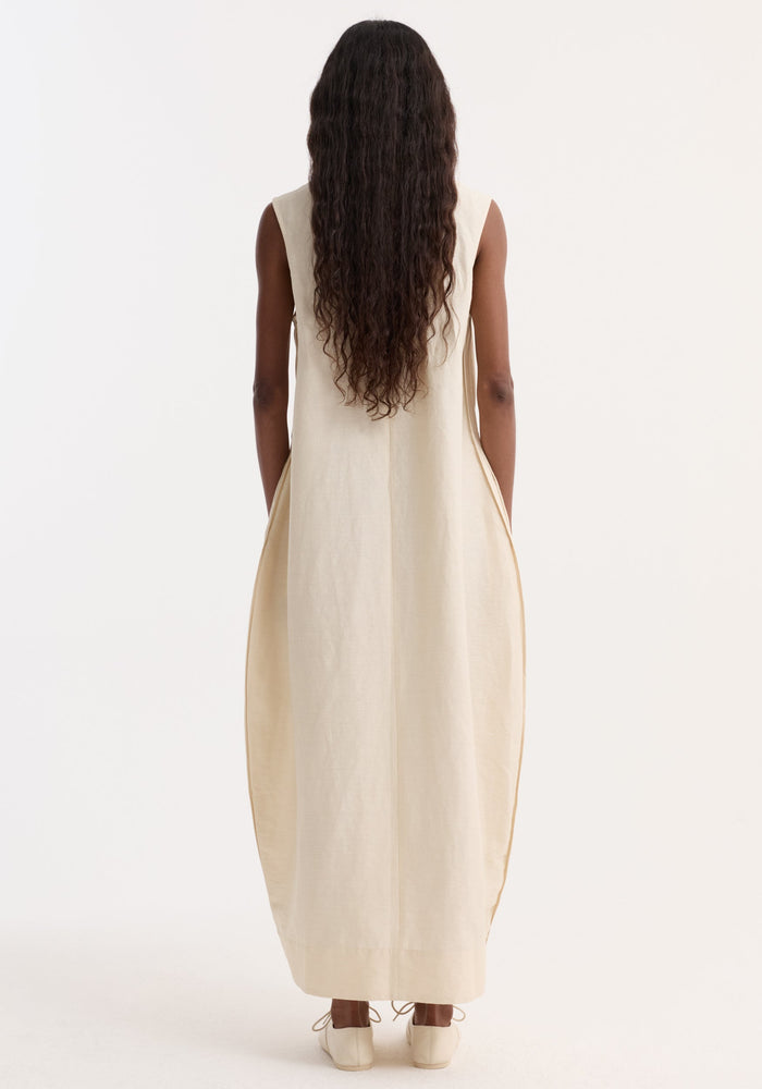 Hourglass linen silk dress | butter, showcased on a model, features a sleeveless, sculptural silhouette with hidden pockets, crafted from a silk-linen blend.
