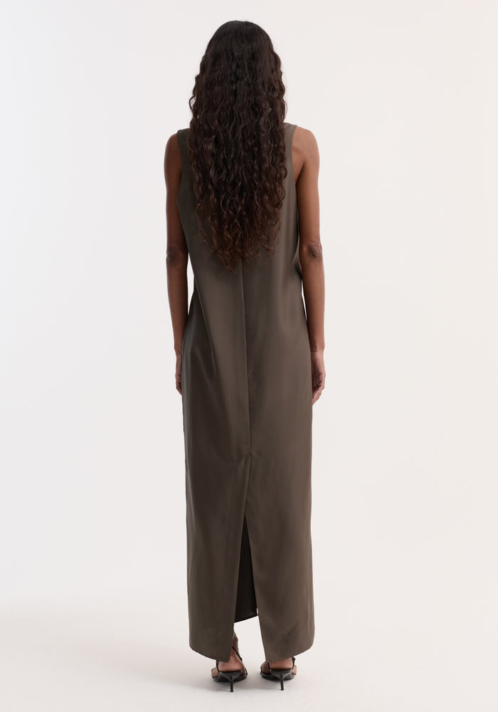 Woman in an olive Silk scoop-neck dress | earth, sleeveless, ankle-length, with a back seam and slit. Her wavy hair cascades, paired with black sandals.