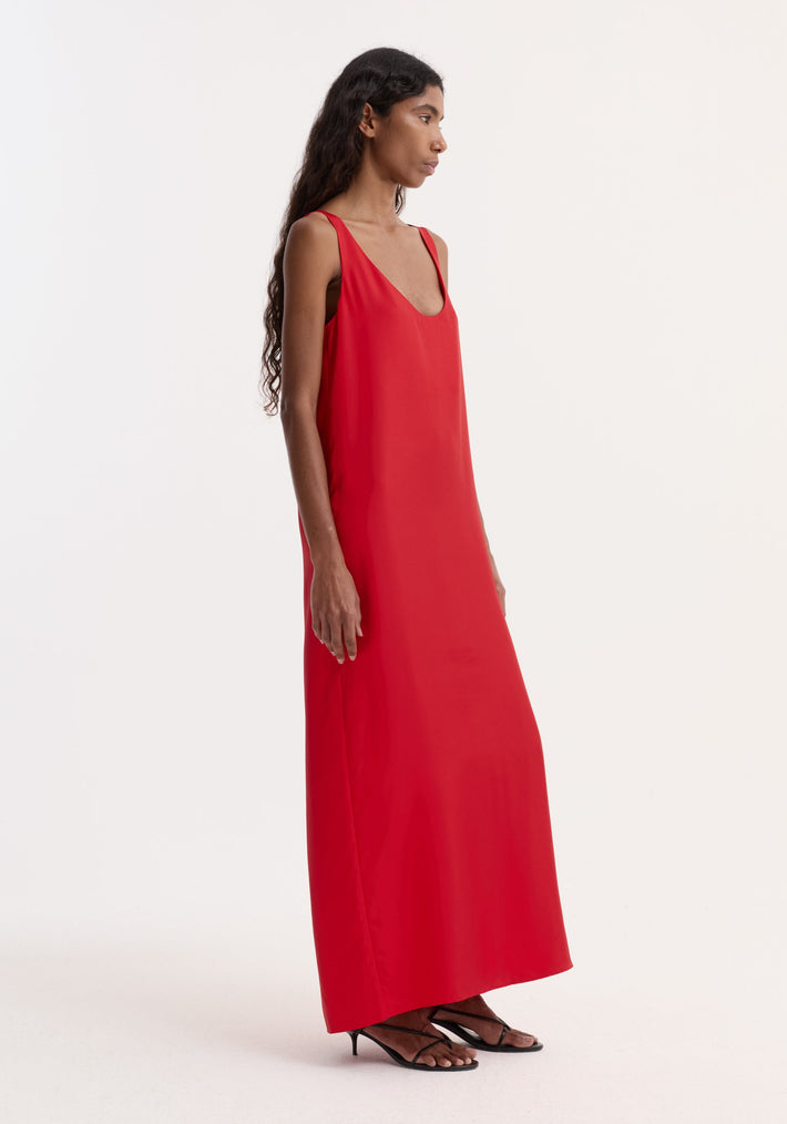 Silk scoop-neck dress in red, worn by a model in profile, features a floor-length, sleeveless design with a relaxed silhouette, crafted from 100% silk.