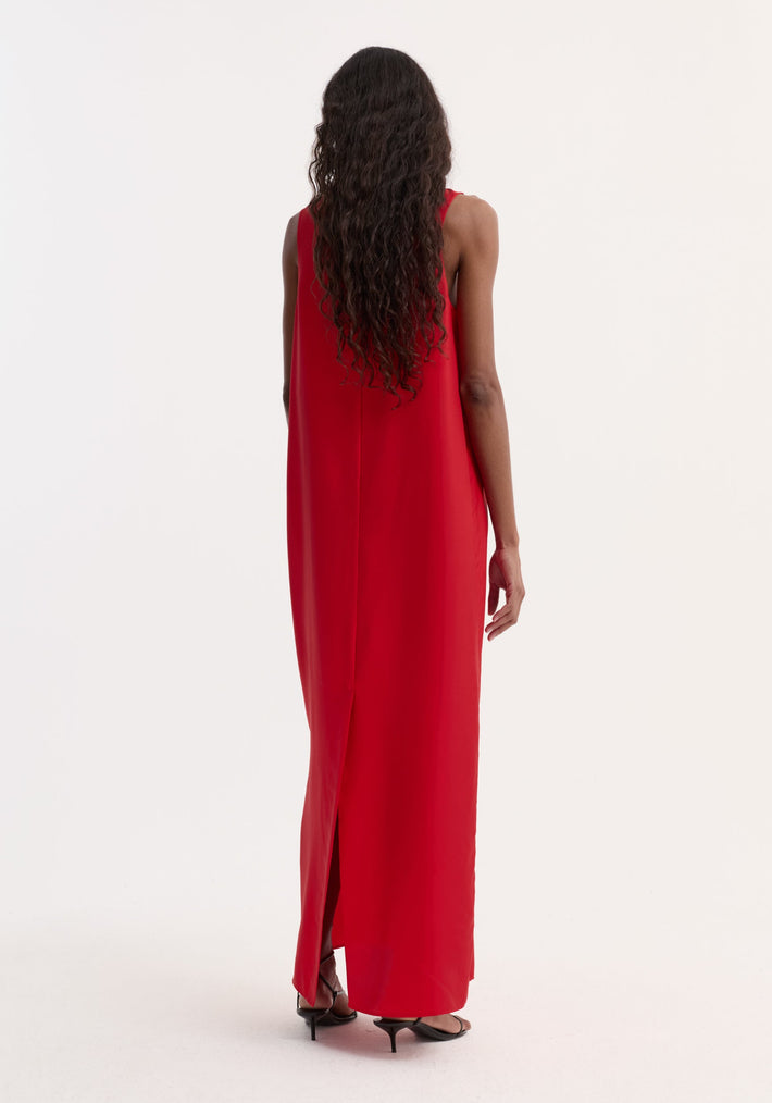 Back view of a model in a Silk scoop-neck dress | red, showcasing its sleeveless, floor-length design with a back slit, paired with black strappy heels.