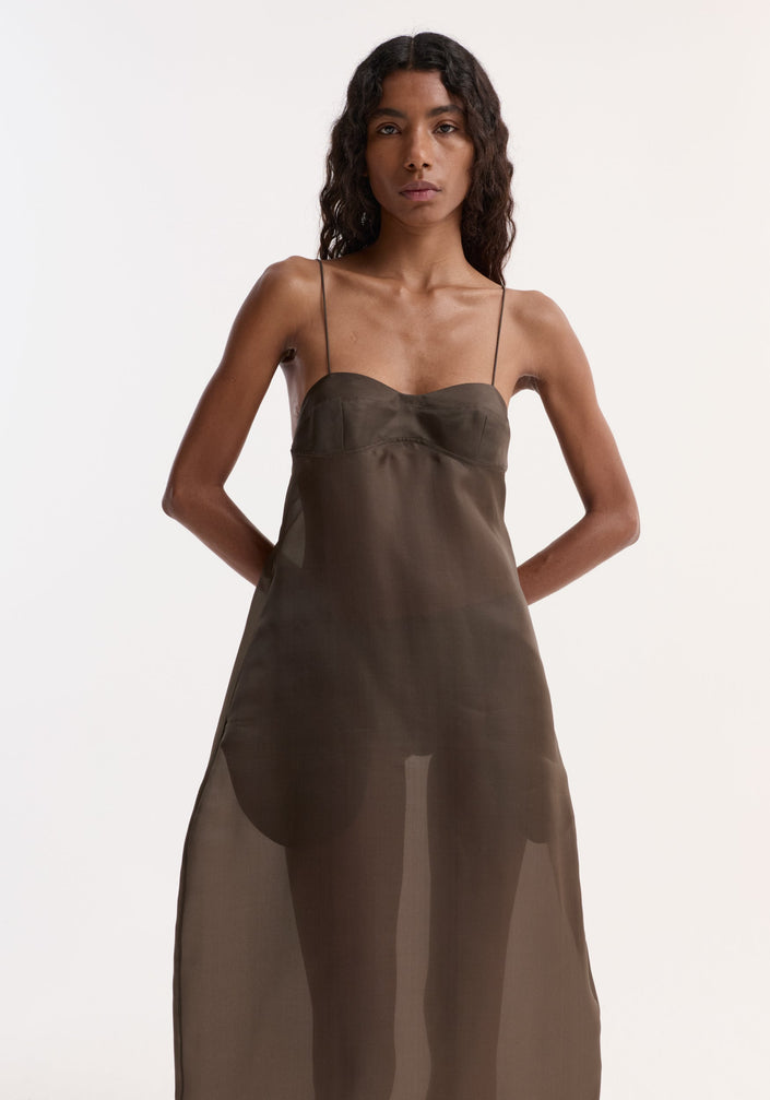 Sheer bustier volume dress | earth, featuring a sheer silk organza design with bustier detailing, adjustable straps, and a full sculptural skirt. Model wears black strappy sandals.