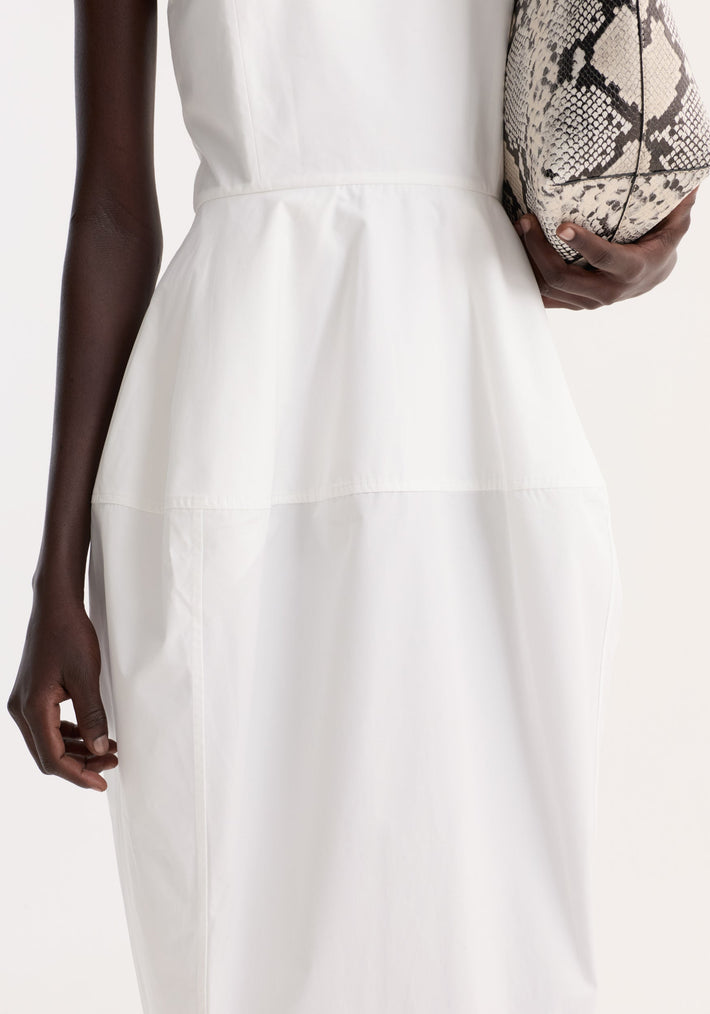 Sculptural poplin dress in optic white, sleeveless with a dropped waist and architectural skirt, held alongside a snakeskin print pouch.