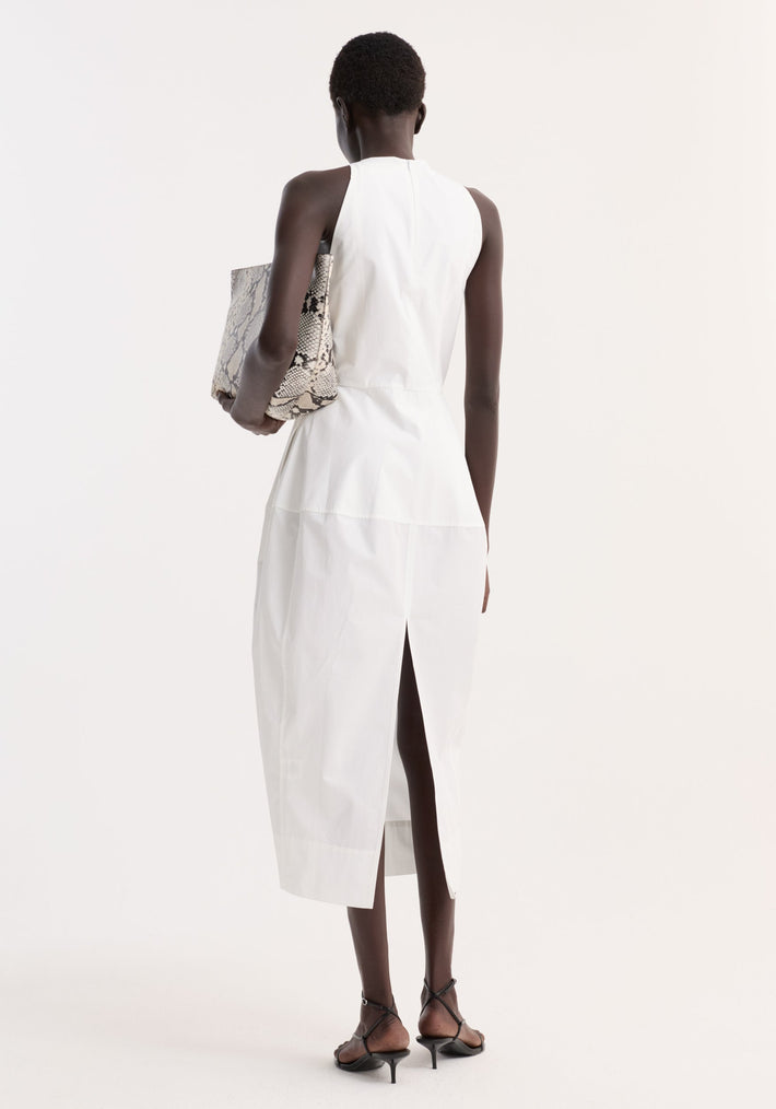 Model wearing Sculptural poplin dress | optic white, featuring a sleeveless design, fitted waist, trapezium skirt, and back slit. Paired with black strappy sandals and a snake-print tote.
