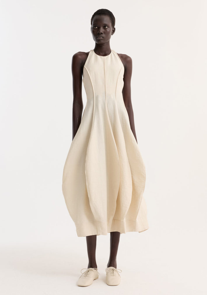 Model wearing the Open Back Tulip Dress | Butter, featuring a halter neck, balloon skirt, and low back, paired with light-beige lace-up flats.