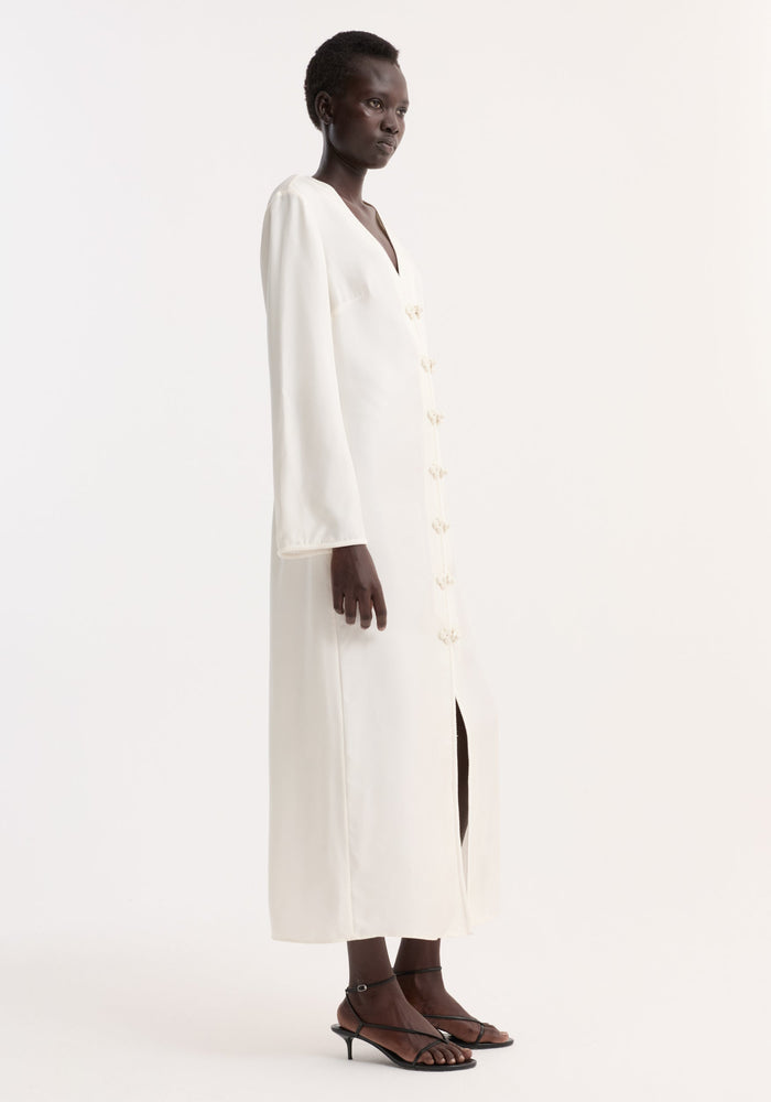 Pankou closure silk dress | cream: A model wears an ivory silk dress with V-neck, pankou buttons, long sleeves, and a front slit, paired with black strappy heels.