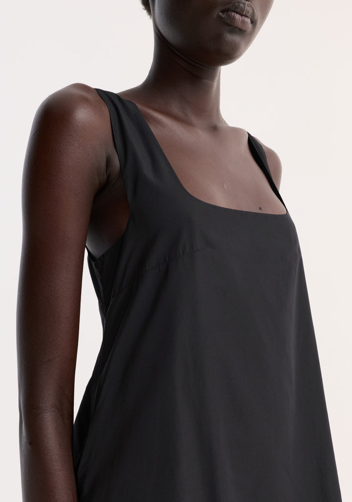 Close-up of a person wearing a Technical volume dress in black, highlighting its sleeveless design, square neckline, and draped fit with a distinctive balloon hemline.