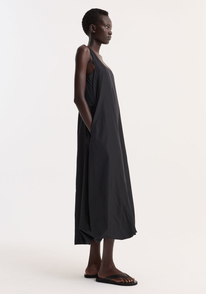Model in profile wearing the Technical volume dress | black, a sleeveless maxi with wide straps, scooped square neckline, balloon hemline, and deep armholes.
