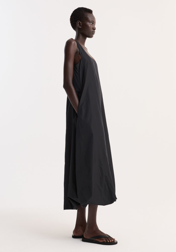 Technical volume dress in black with a sleeveless design, scooped square neckline, and balloon hemline. Model wearing size 34 with hand in hidden pocket.