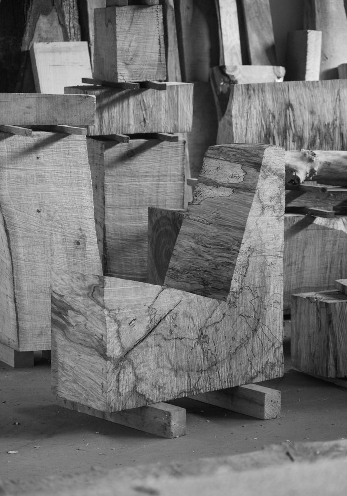 Brutalist Chair | 5788: L-shaped oak block with visible grain and spalting, showcasing rough chainsaw cuts, emphasizing the raw beauty and functionality in a workshop setting.