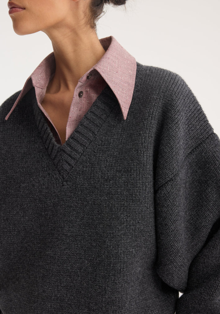 Close-up of a model wearing a Sculptural compact V-neck sweater in charcoal-gray, layered over a pink collared shirt, showcasing its relaxed fit and expert Italian wool knit.