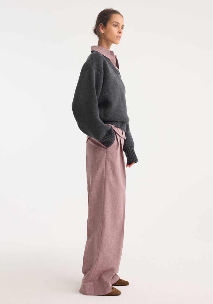Woman wearing Sculptural compact v-neck knit in mid grey melange, styled over a collared shirt with wide-leg trousers, embodying relaxed, editorial elegance.