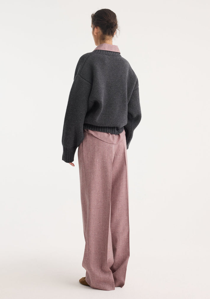 Woman wearing Sculptural compact v-neck knit in mid grey melange over a rose-pink shirt, paired with matching wide-leg trousers, showcasing a relaxed, layered look.