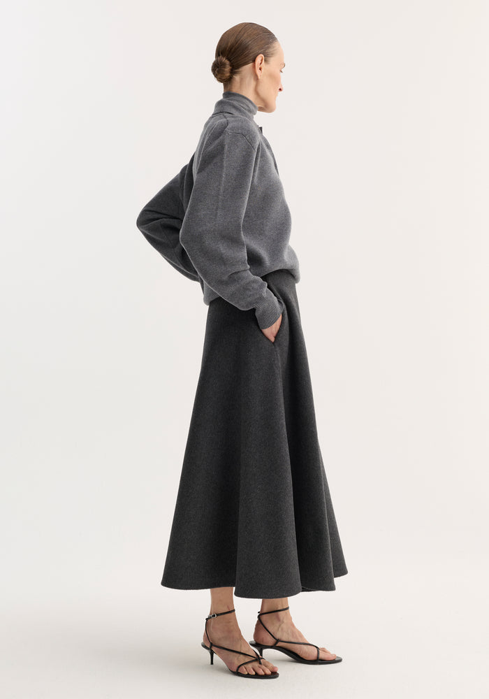 Side-profile of a model wearing the anthracite melange A-line skirt, showcasing its flared, mid-length design with seamless zipper and side pockets.
