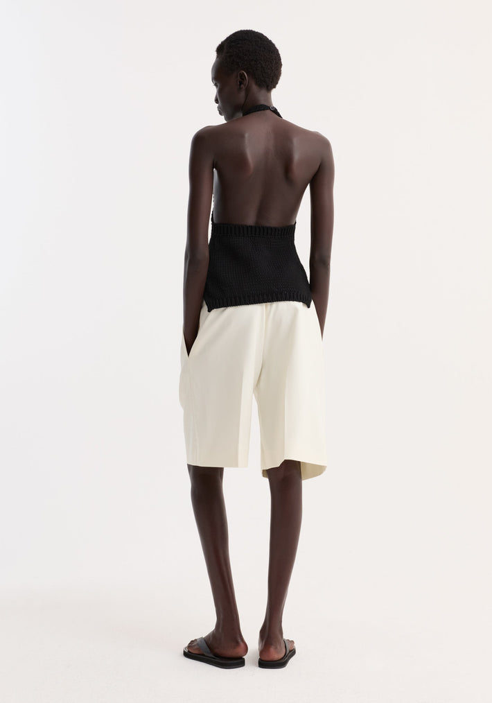 Model in Chunky knit halter top | black, showcasing the exposed back, loose knee-length shorts, and flat slide sandals, emphasizing minimalist design and comfort.