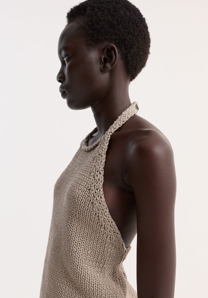 Chunky knit halter top worn by a woman, showcasing its sleeveless design, side slits, and button neck closure, made from 100% cotton.