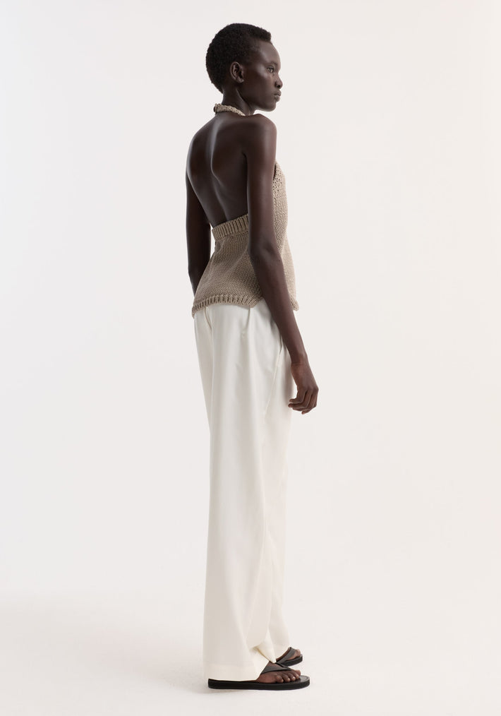 Model in profile wearing the Chunky knit halter top | stone with side slits and button neck, paired with high-waisted wide-leg trousers and black sandals.