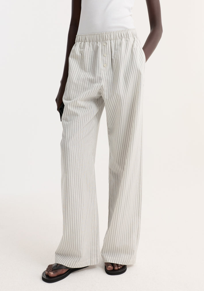 Silk stripe pyjama trousers featuring pinstripes, elasticated waistband, and faux fly. Paired with black sandals and a white tank tucked in.