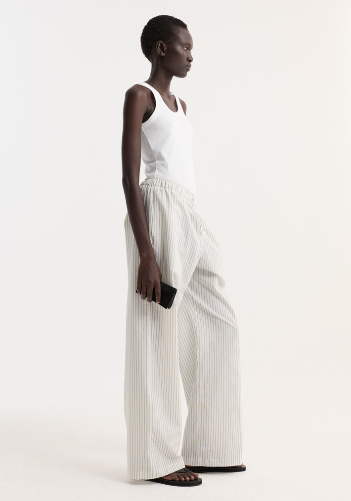 Model in profile wearing Silk stripe pyjama trousers with wide-leg design, elasticated waistband, and faux fly, paired with a white ribbed tank top and black sandals.
