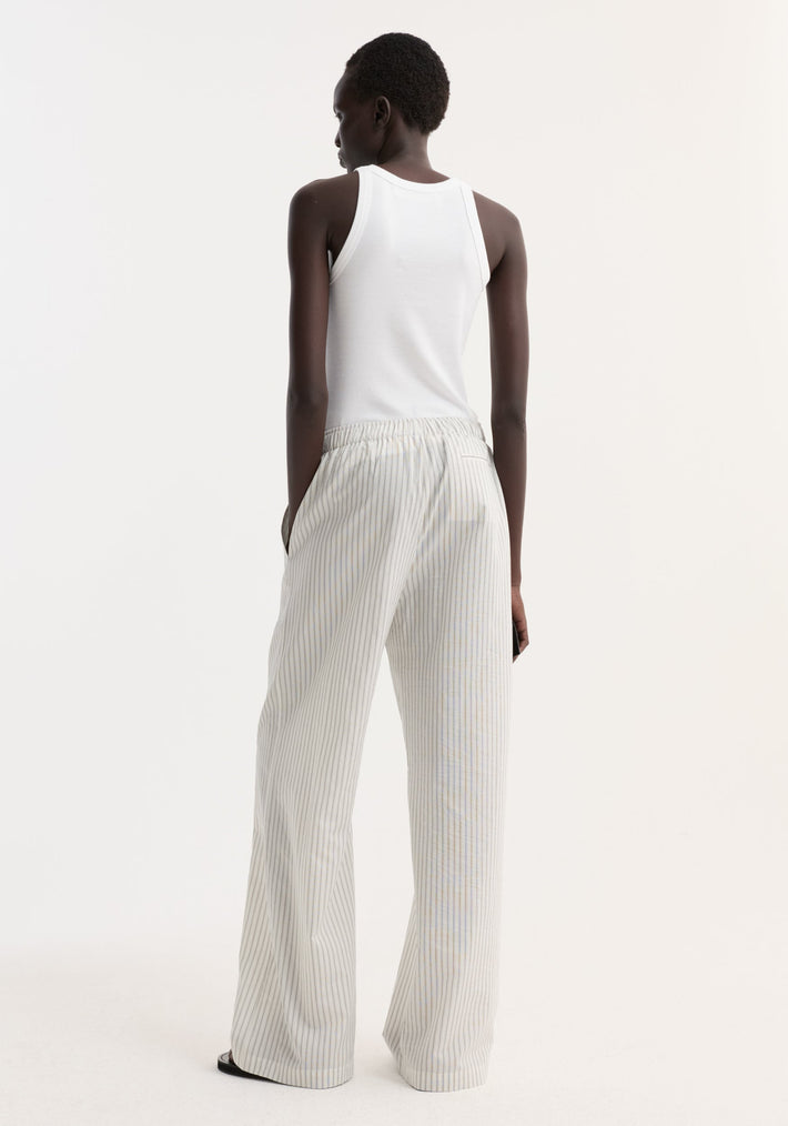 Silk stripe pyjama trousers with elastic waistband, wide-leg fit, faux fly, and two-button detail, worn by model with hands in pockets.