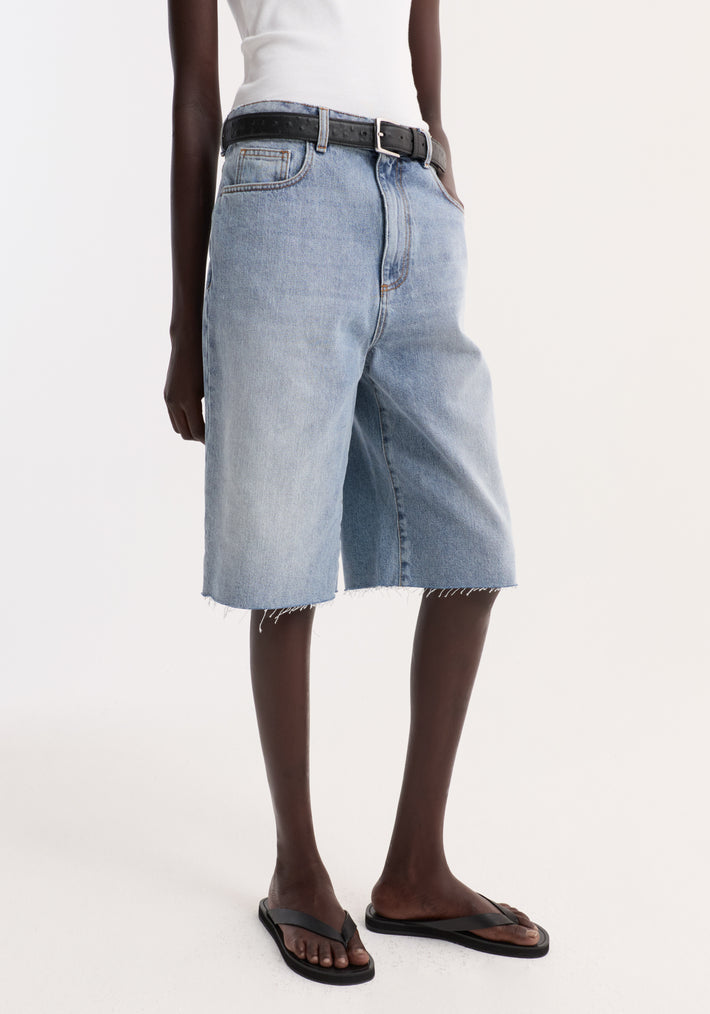 Baggy fit denim shorts in classic blue with a raw-edge hem, worn with a black belt and flip-flops, showcasing a relaxed, casual style.