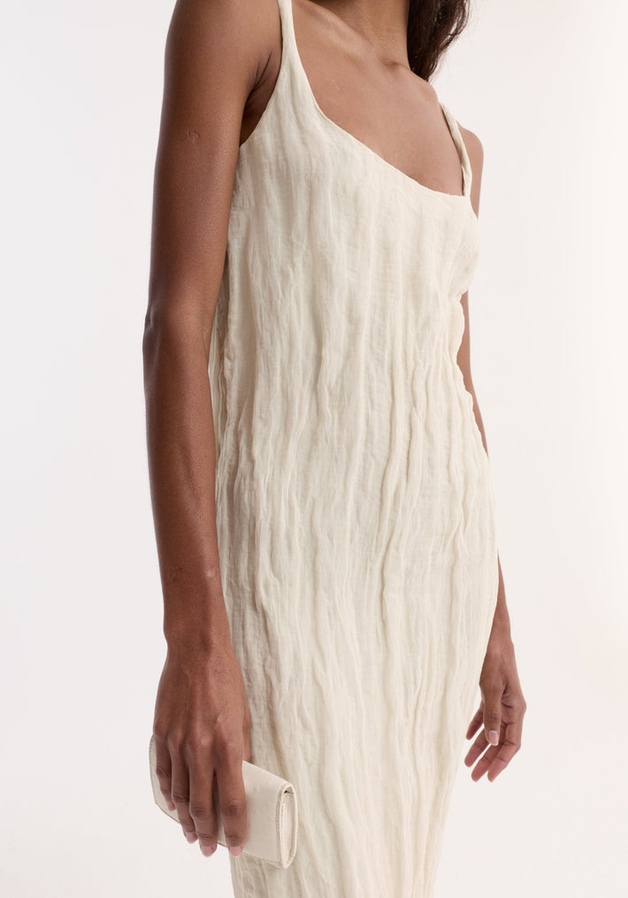 Textured square neck dress | cream slip dress with thin straps, featuring a crinkled finish. The model holds a matching clutch in a simple studio setting.