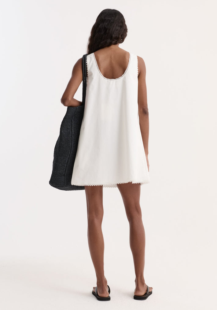 A-line poplin mini dress in optic white, featuring scalloped scoop back, delicate embroidery, and a-line silhouette, paired with black tote and slide sandals.