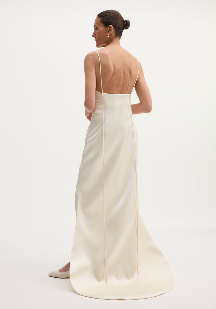 Woman in Satin bustier dress with train, wearing ivory slip dress, spaghetti straps, fitted waist, slicked-back hair, and small earrings, photographed from behind.