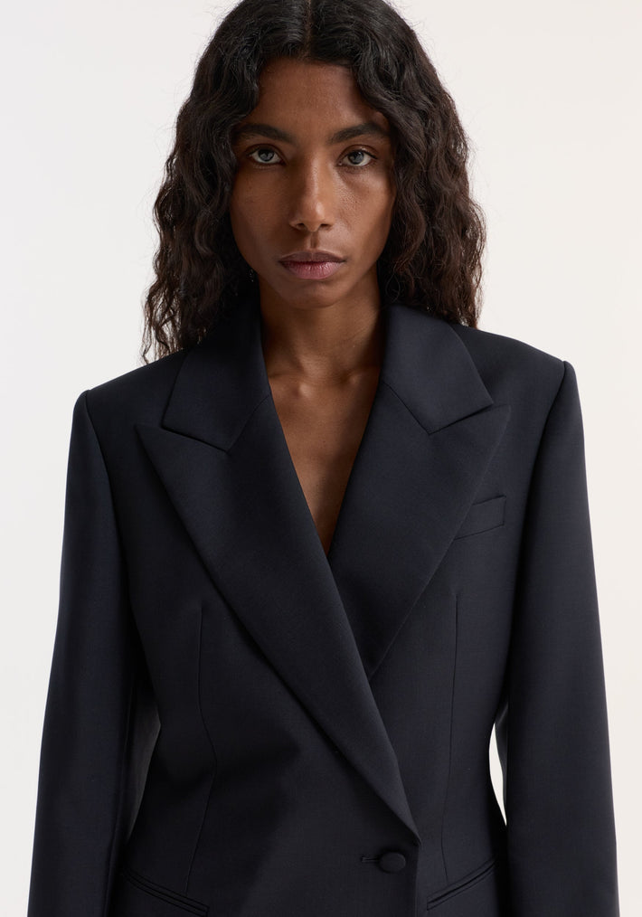 A model wears an Hourglass shaped blazer, showcasing its sharp notch lapel and cinched waist, highlighting its sleek, tailored fit and architectural silhouette.