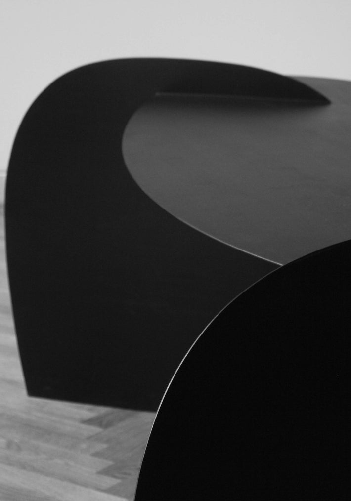 Sculpted Table | 9845: A sleek, ribbon-like oak wood sculpture by Arne Kristian, curving elegantly on a parquet floor in a minimalist gallery setting.