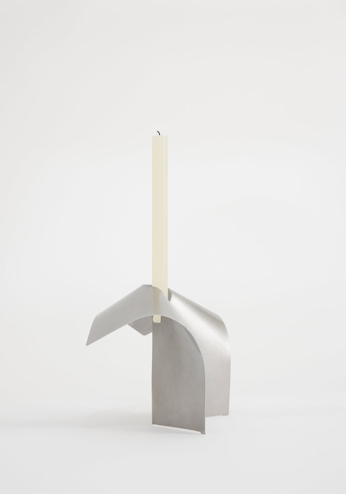 Stainless steel candle holder featuring a minimalist, interlocking design by Dutch designer Paul Coenen, showcasing a handcrafted, sculptural stand with an ivory taper candle.