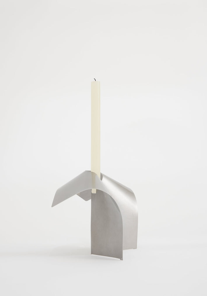 Stainless steel candle holder featuring a minimalist, interlocking design by Dutch designer Paul Coenen, showcasing a handcrafted, sculptural stand with an ivory taper candle.