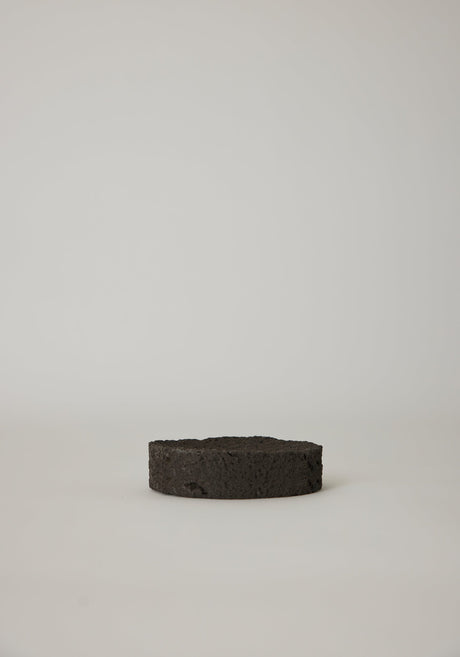 Round Tray handcrafted from lava stone, featuring a carved indent, shown with wooden sticks on a marble windowsill. Unique and available on request.