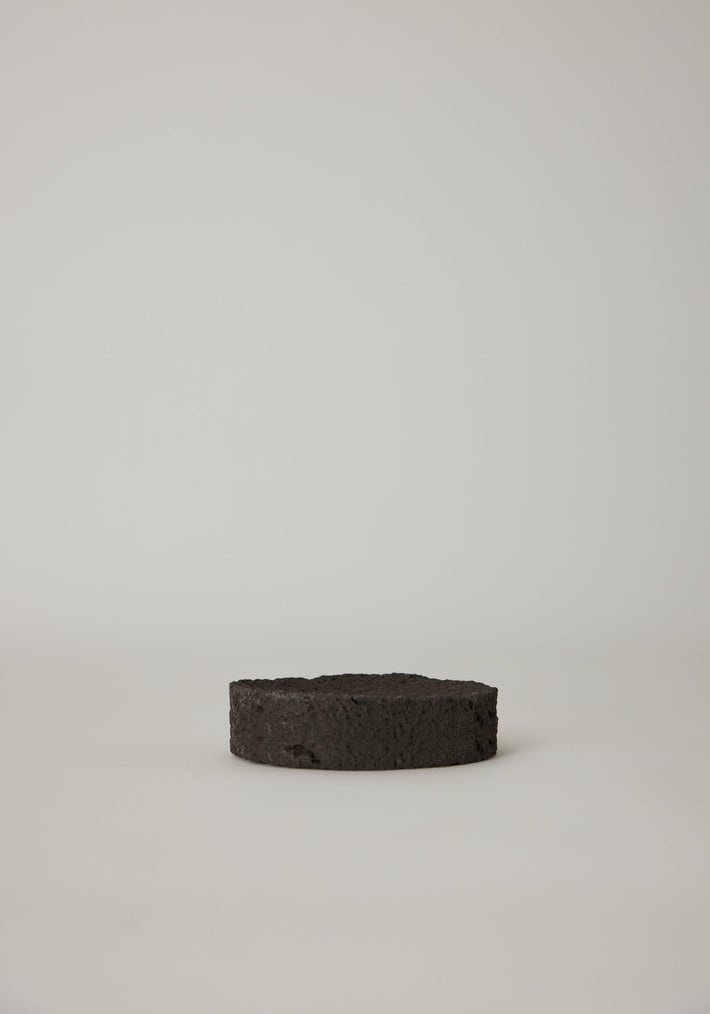 Round Tray crafted from leftover lava stone, appears as a porous black disc. Handcrafted by Louis Crombag, each unique piece measures 2 cm high and 13.5 cm wide.