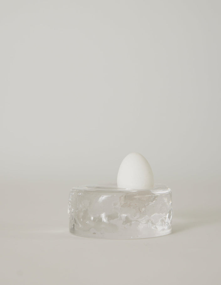 Presse-papier & holder | Glass: A single white egg stands on a transparent glass block, showcasing Szkło Studio's unique hand-blown craftsmanship and experimental design.