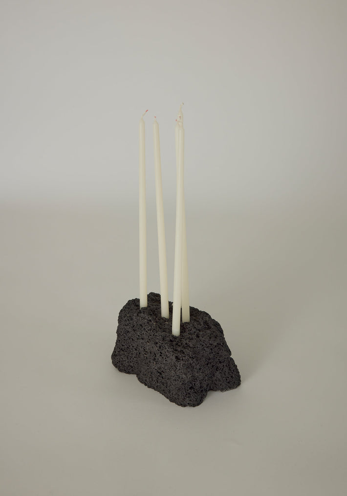 Sculptural Stone Candle Holder: A black, porous lava stone block with four white taper candles, handcrafted by Louis Crombag, showcasing minimalist Dutch design.