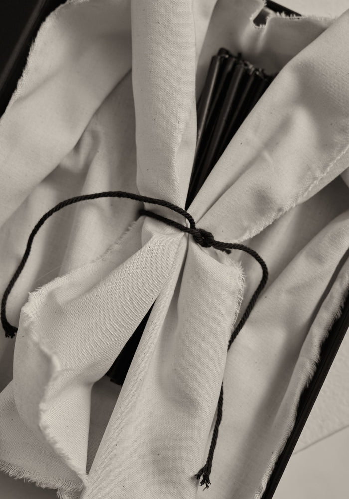 Close-up of Candles 10mm | noir, wrapped in white cloth, tied with black cord, partially revealing black rib-like slats, suggesting a folded hand-fan.