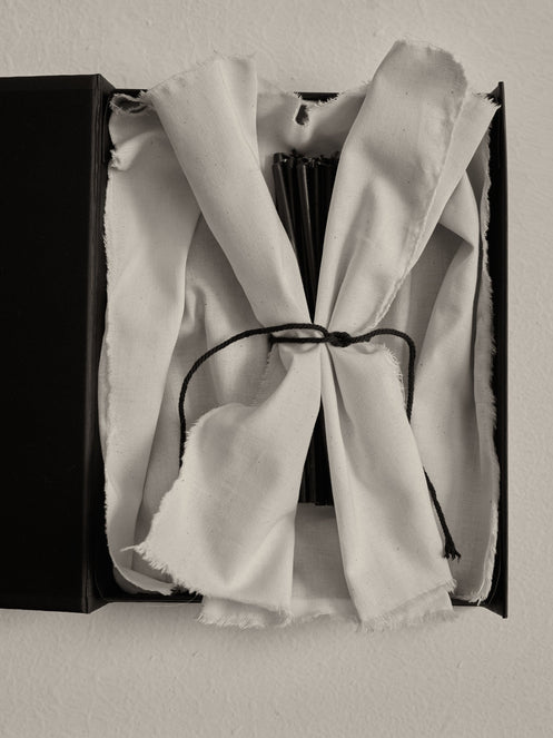 Candles 5mm | noir: A black box with a tied white-cotton cloth revealing a bundle of 30 slender, 10 cm tall beeswax candles.