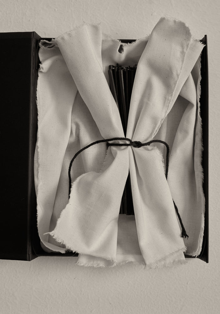 Candles 5mm | noir: A black box with a tied white-cotton cloth revealing a bundle of 30 slender, 10 cm tall beeswax candles.