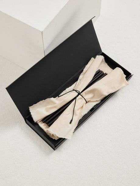 Candles 10mm | noir: A long black gift box with off-white cloth holds slender matte-black beeswax candles, tied with a dark cord, ideal for gifting.