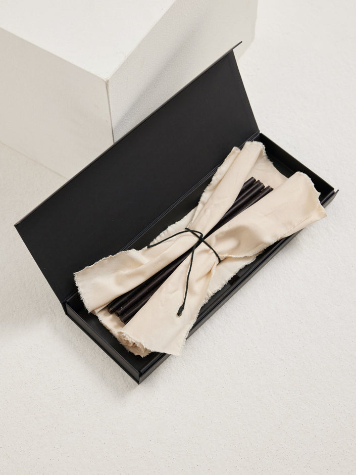 Candles 10mm | noir: A long black gift box with off-white cloth holds slender matte-black beeswax candles, tied with a dark cord, ideal for gifting.
