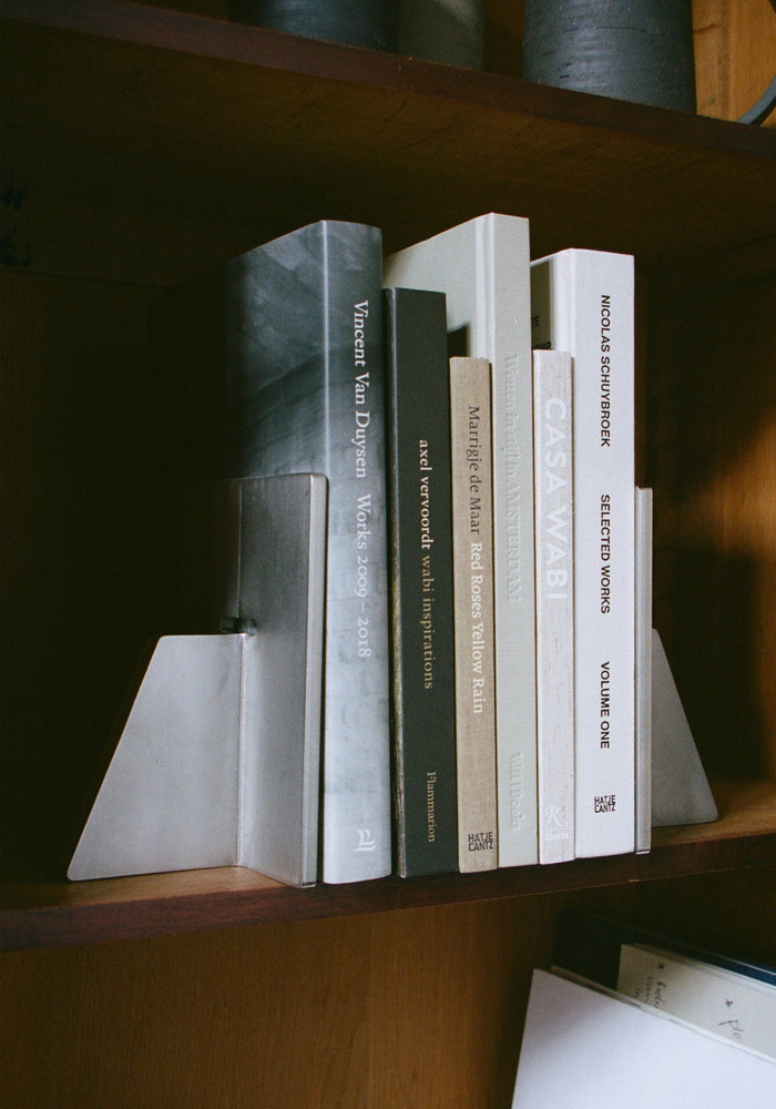Stainless steel bookends holding architecture books on a wooden shelf, featuring minimalist design, crafted by Paul Coenen from 8mm thick stainless steel.