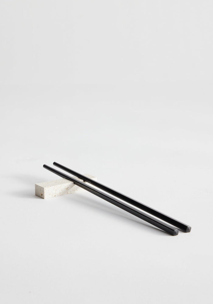 Chopstick holders | travertine, featuring a black chopstick on a handcrafted stone rest made from Italian travertine, showcasing artisanal Dutch craftsmanship by Louis Crombag.