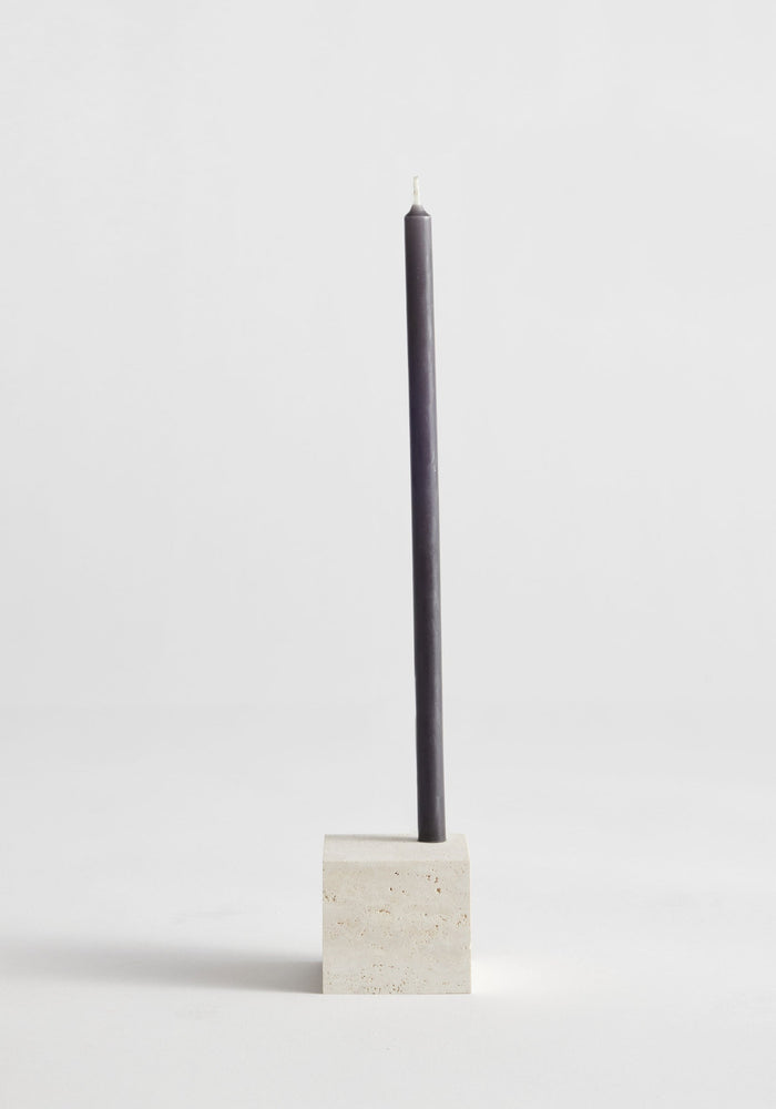 Two-way cube candleholder in travertine, showcasing a dark taper candle. Handcrafted by Louis Crombag, highlighting its dual candle sizing feature and minimalist design.