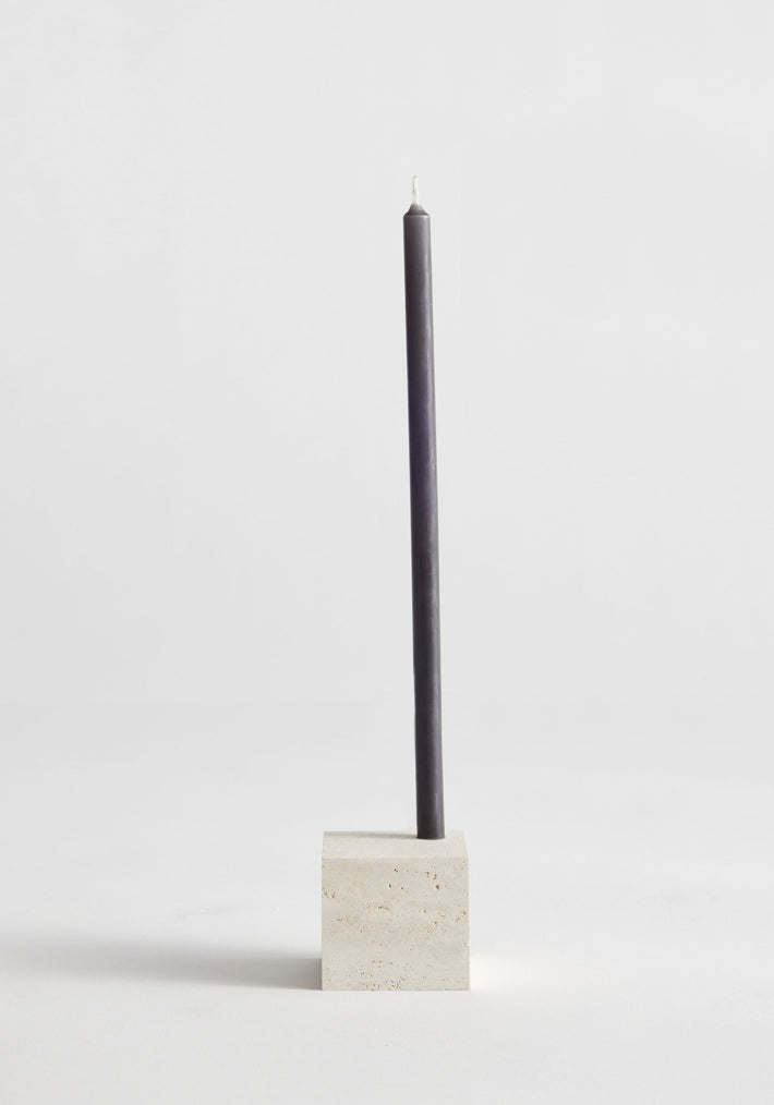 Two-way cube candleholder in travertine, showcasing a dark taper candle. Handcrafted by Louis Crombag, highlighting its dual candle sizing feature and minimalist design.