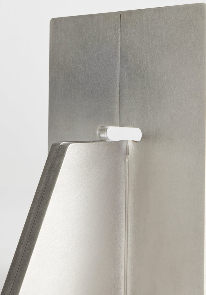 Close-up of stainless steel bookends with a white spacer insert, showcasing the handcrafted design by Paul Coenen, emphasizing the brushed metal finish and precise craftsmanship.