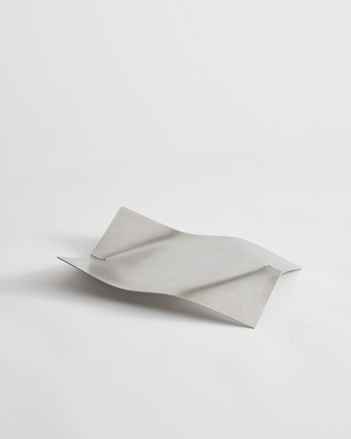 Stainless steel bowl in a wave shape, handcrafted from a single sheet, showcasing a minimalist design by Dutch designer Paul Coenen, on a white background.